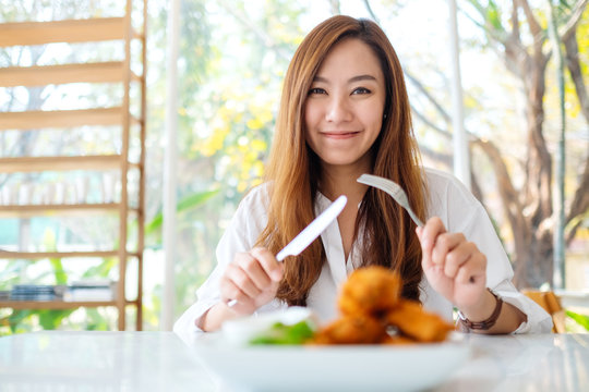 Closeup image of a beautiful asian woman using knife and fork to eat fried chicken in restaurant