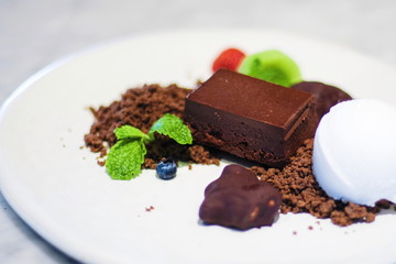 Close up sweet dessert brown pieces of chocolate and vanilla ice-cream with mint leaves on white plate.