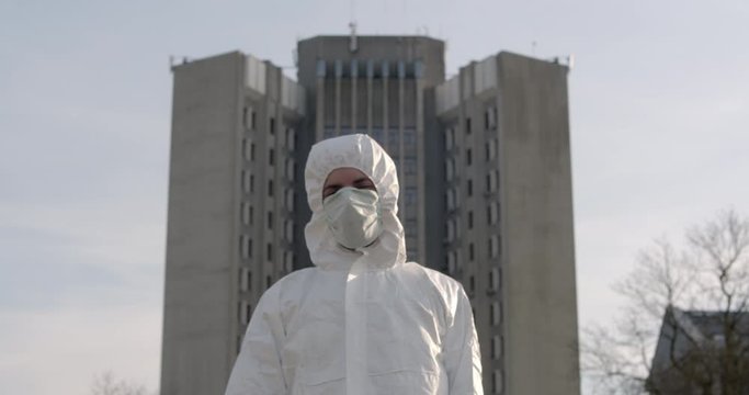 Portrait of happy male scientist in protective suit standing and showing thumbs up in daytime street after pandemic coronavirus quarantine ends with big cityscape buildings in background 4K