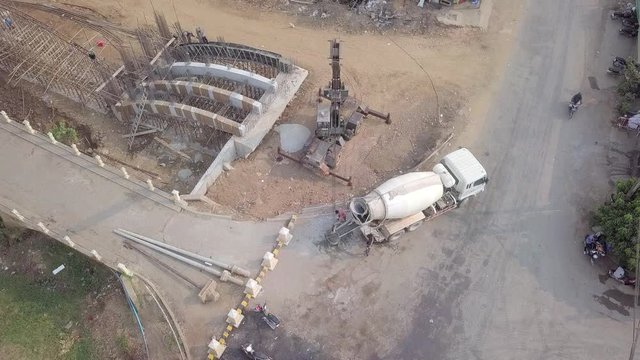 Aerial static view of a concrete mixer truck pouring concrete into a bucket and it being lifted by a crane. Bridge under construction