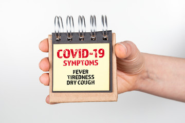 COVID-19 SYMPTOMS. Fever, tiredness and dry cough. Note book in hand