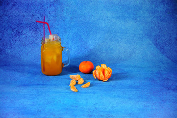 Glass mug of citrus juice with ice and ripe tangerine nippers on a blue background. © Алексей Желтухин