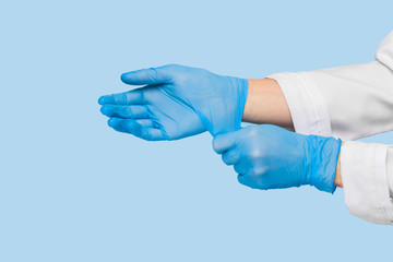 The doctor puts on sterile gloves on a blue background. Infection control concept. Danger of spread...