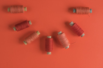 A coral spool of threads on coral paper background, with copy space.