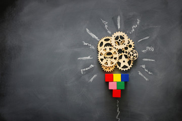 Education concept image. Creative idea and innovation. Wooden gears light bulb metaphor over blackboard - obrazy, fototapety, plakaty