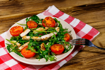 Tasty salad of fried chicken breast, fresh arugula and cherry tomatoes on wooden table
