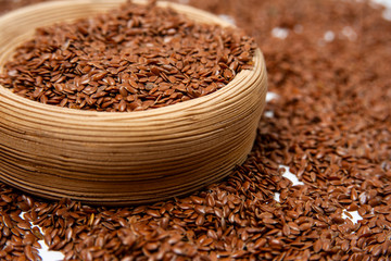 heap of flax seeds lies on a white background and in a light brown ceramic bowl