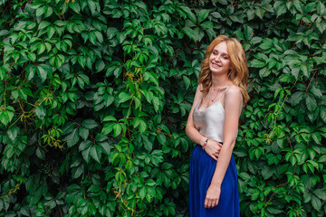 Portrait of a young beautiful woman, standing next to the wall of wild grape leaves.