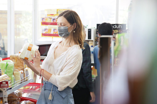  Woman wearing protective mask while grocery shopping in supermarket, Coronavirus contagion fears concept	