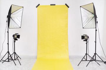 Empty studio with yellow backdrop and light equipment. Copy​ space​ for​ text or​ mock-up