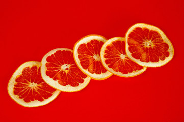 Chips of dried grapefruit sliced in thin circles, shot on a red background. Background for vegetarianism, healthy and wholesome food.