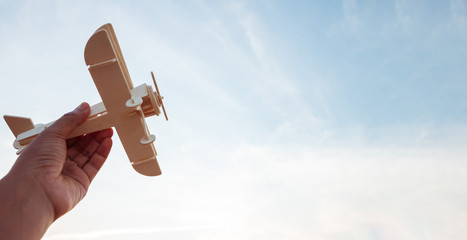 Freedom concept, human hand holding wooden plane on the sunset sky background