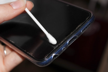 Hand with a cotton swab to clean the smartphone screen, the concept of phone hygiene, virus prevention.