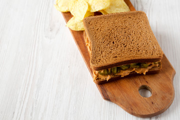 Fototapeta na wymiar Homemade Peanut Butter Pickle Sandwich with Potato Chips on a rustic wooden board on a white wooden background, side view. Copy space.