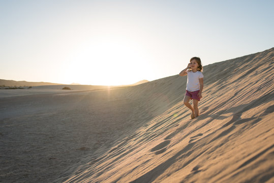 Lovely little girl walking on sand dune and making phone calls.