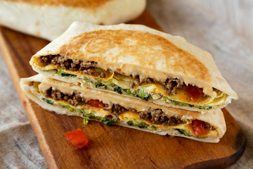 Tasty Homemade Beef Crunchwrap Quesadilla on a rustic wooden board on a white wooden surface, low angle view. Close-up.