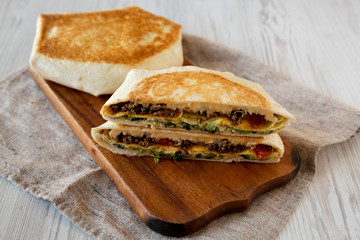 Tasty Homemade Beef Crunchwrap Quesadilla on a rustic wooden board on a white wooden background, low angle view.