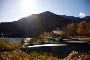 Cena de lago com barcos encalhados na beira, uma casa e montanhas no fundo.