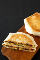 Tasty Homemade Beef Crunchwrap Quesadilla on a rustic board on a black surface, high angle view. Copy space.