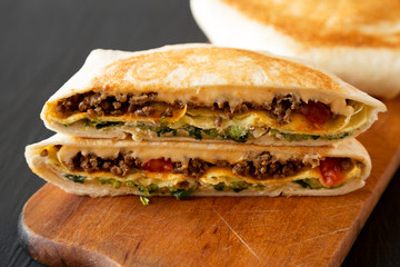 Tasty Homemade Beef Crunchwrap Quesadilla on a rustic board on a black background, low angle view. Close-up.