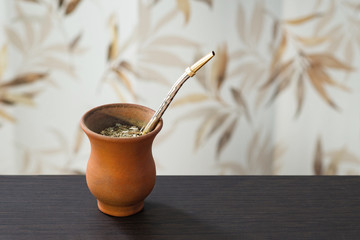 Yerba mate with bombilla in clay calabash on wooden table