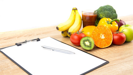 Fresh colorful vegetables, organic fruits and juice on wooden table with clipboard, paper and pen, white background with copy space for text. Cooking ingredients, healthy food and nutrition concept.