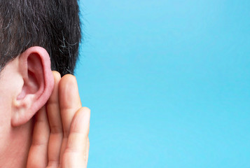 Obraz premium The man listens attentively with her palm to her ear close-up, blue background
