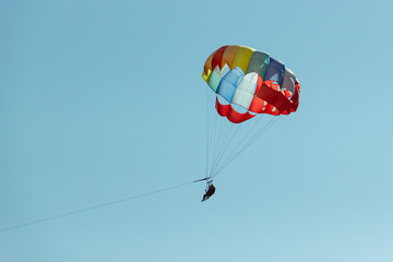 With a parachute for parasailing a couple flies through the air with blue sky in the background. Happy couple hovers in the air on a multi-colored parachute and admires the scenery from a bird 's eye