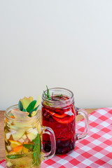 Set of 2 different hot drinks on plaid table, white background. Tea with ginger, lemon, orange, mint.