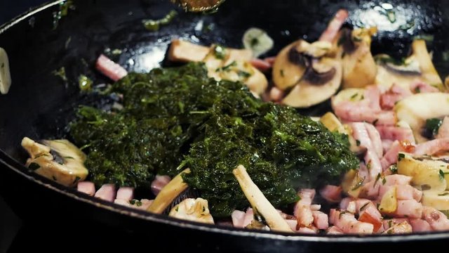 Finely chopped ham, garlic, mushrooms and spinach is fried in hot oil in a pan.
