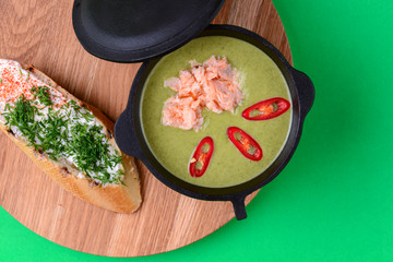 Salmon soup served in a bowl with a cream cheese bruschetta on a rustic wooden board over bright green background.