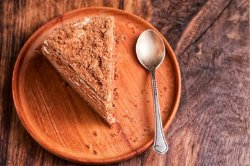 A piece of homemade honey cake, on a wooden plate and an old teaspoon. On an oak table