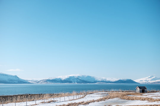 Tromso, Norway - April 29 2018: Isolated abandoned hut on fjord shore in a clear sunny day with mountains in the background 