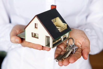 A close up shot of a person's hands holding a miniature house and keys - real estate concept