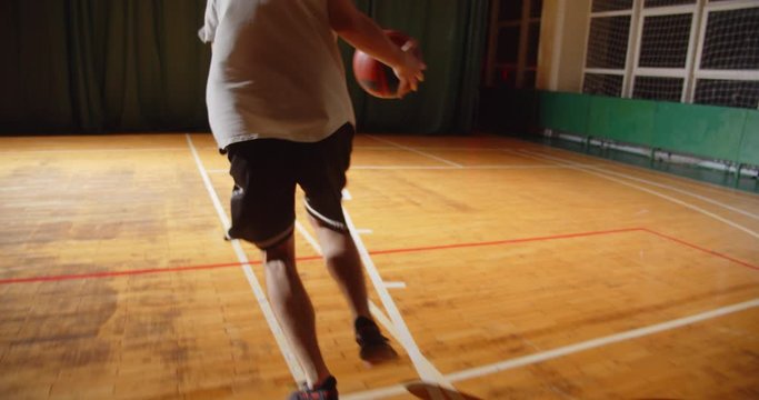 Young Caucasian basketball player plays throwing the ball into the basket night darkness silhouette rear view dribbling close-up parquet endurance