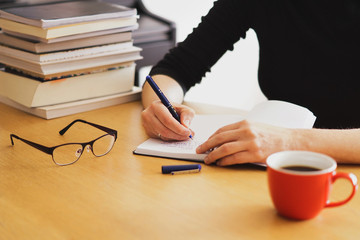 A woman taking notes in her notebook with a cup of coffee nearby