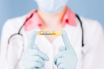 young doctor holding an antidote to coronavirus in his hands in a uniform in a mask with gloves on a blue background