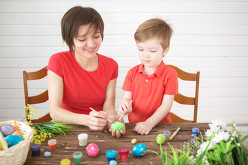 Naklejka premium Easter preparations. Happy young mother spending time with her joyful son. Happy family Mom and children son paint easter eggs with colors. Preparation for holiday.