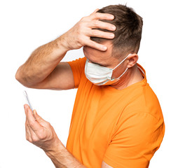 Man in mask holding thermometer in hands, measuring body temperature while suffering from influenza