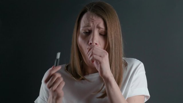 A young girl uses an electronic cigarette and coughs