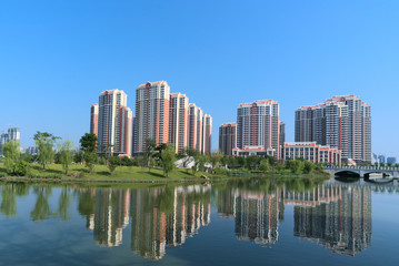 Obraz na płótnie Canvas Beautiful city park. High-rise buildings reflecting on calm lake with blue background