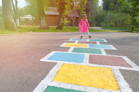 Little girl in a pink dress playing hopscotch on playground outdoors, children outdoor activities
