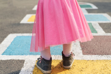 Little girl in a pink dress plays hopscotch on the street.