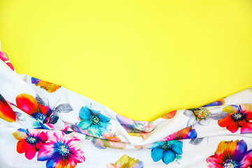 A patch of white fabric with multicolored flowers with drapery on a bright yellow background. Space for text