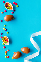 Easter background with chocolate eggs and dragees on blue background top-down frame copy space