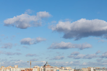 Fototapeta na wymiar tops of city roofs and construction crane over blue cloudy sky.