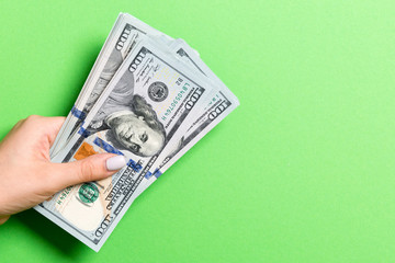 Top view of female hand giving one hundred dollar bills on colorful background. Charity and donation concept with copy space