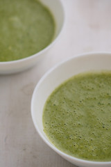 Spring detox broccoli green cream soup in white plates, bowl with crackers and stylish black cutlery on grey background. 