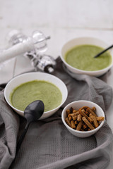 Spring detox broccoli green cream soup in white plates, bowl with crackers and stylish black cutlery on grey background. 