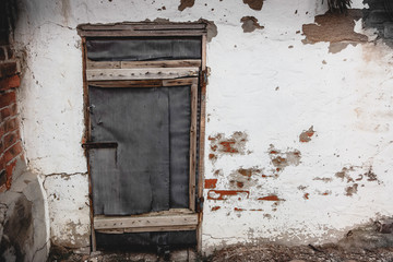Fototapeta na wymiar Old white wall of a house with peeling paint and an old closed door. Decrepit building.